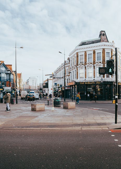 A busy street scene on Bromley High Street during daytime, showing a mix of pedestrians walking on the pavement and vehicles, including cars and vans, moving through the intersection. There is a promi