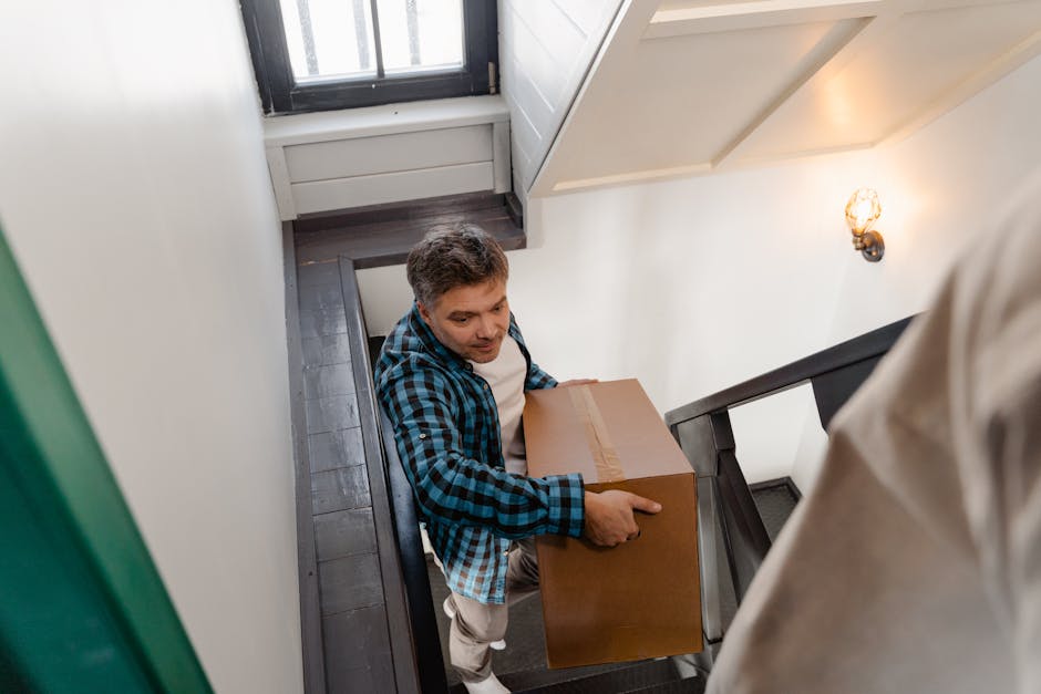 A narrow, outdoor metal staircase with wooden steps and a metal railing, located between two brick and concrete walls, leading up to a higher level with an open landing. The staircase is part of a bui